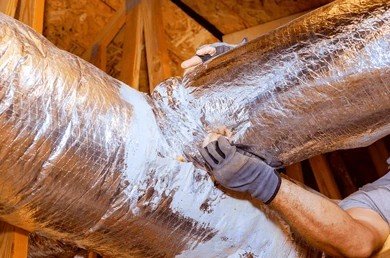 Technician inspecting insulated attic ventilation ductwork for moisture condensation and roof leaks in New Jersey.