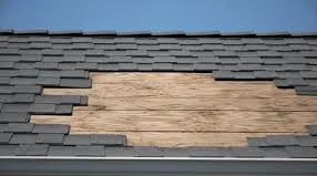 Exposed roof deck under missing asphalt shingles damaged by strong storm winds.