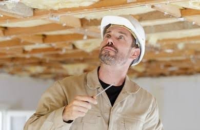Professional contractor wearing hard hat inspecting attic roof rafters and insulation for leaks.